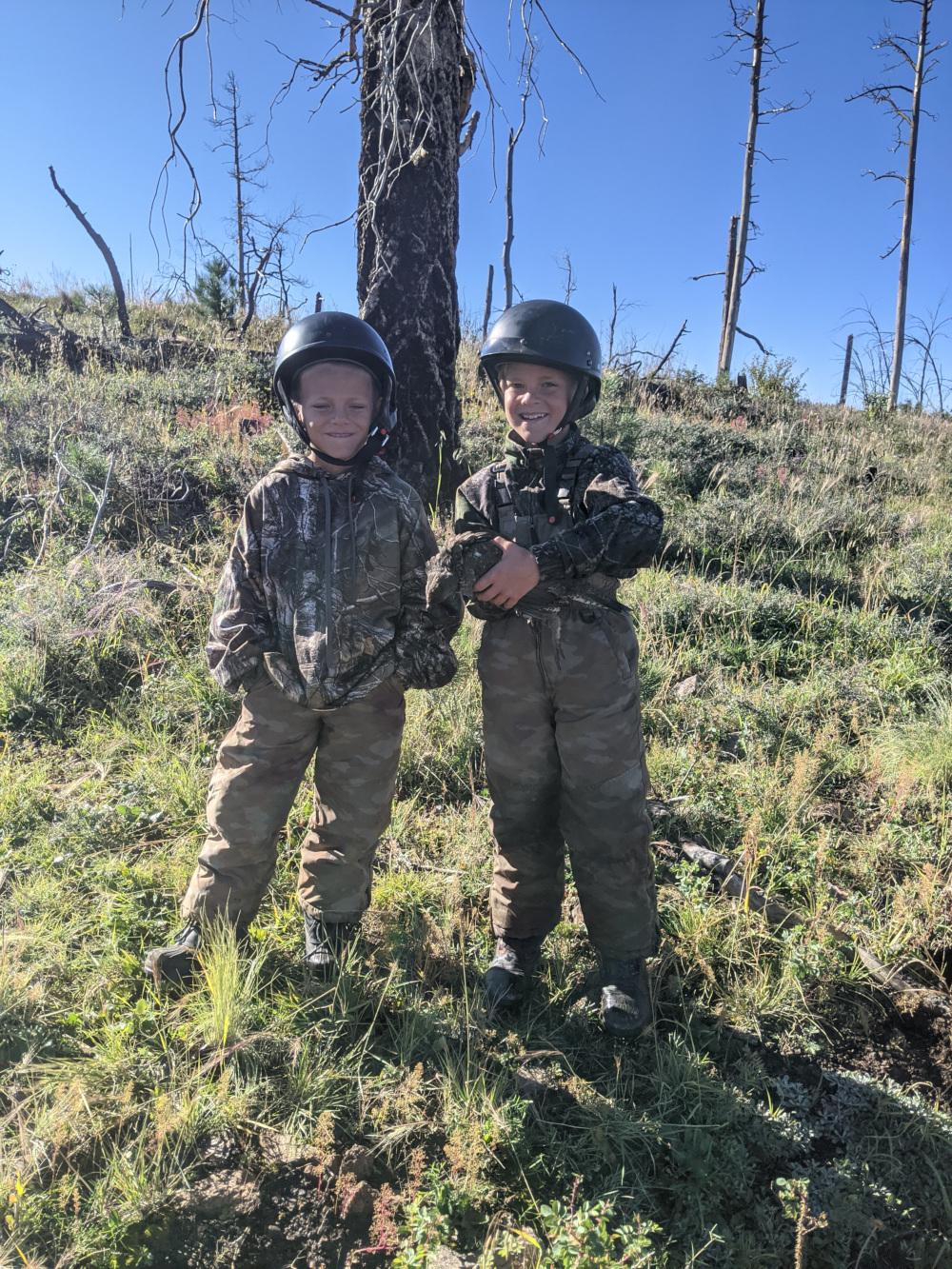 Two young hunters on an Arizona mountainside, one holding the blue grouse they took.